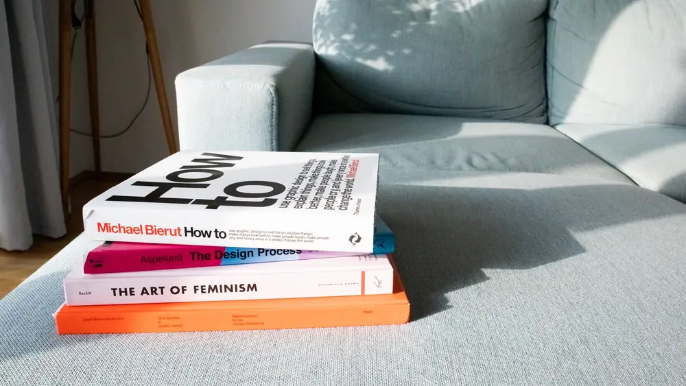 Close-up of design and art books on a modern sofa in a sunlit living room.