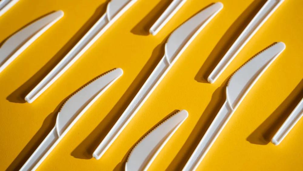 Minimalist arrangement of white plastic knives on a bright yellow background.