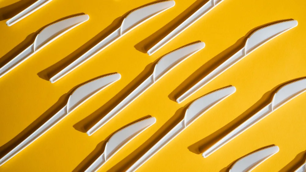 White plastic knives arranged on a vivid yellow background, emphasizing minimalism and texture.