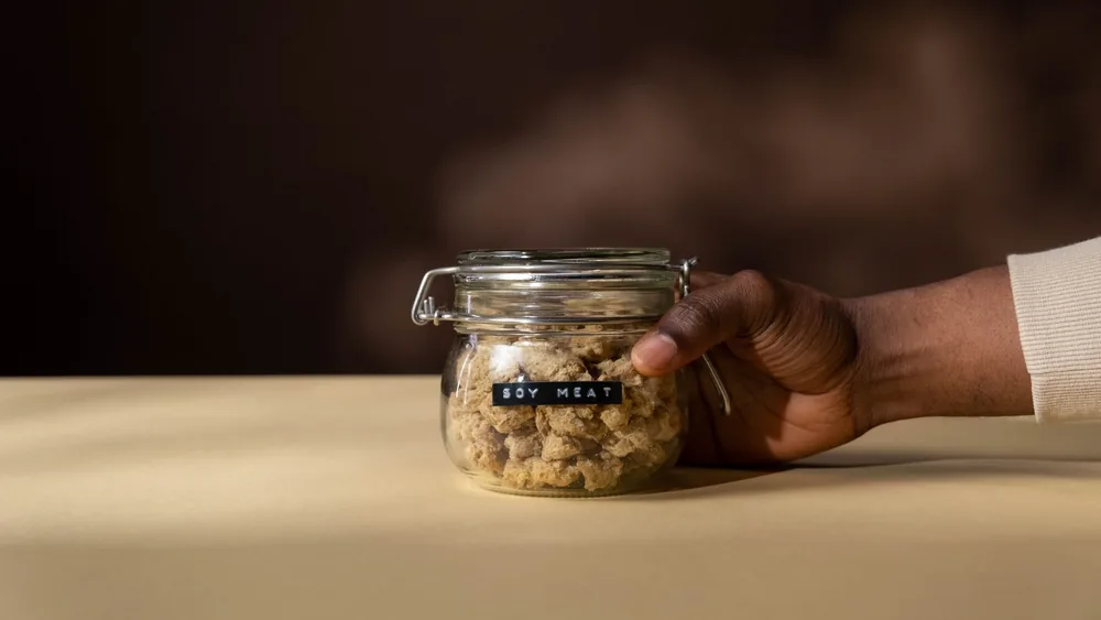 Glass jar of soy meat held in hand, emphasizing vegan nutrition and product photography.
