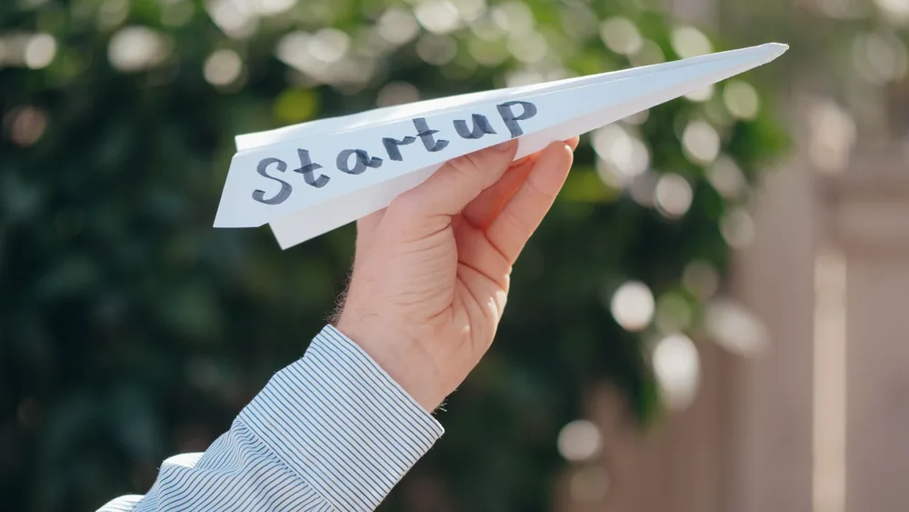 Close-up of a hand holding a paper plane with 'Startup' written, symbolizing a business launch.
