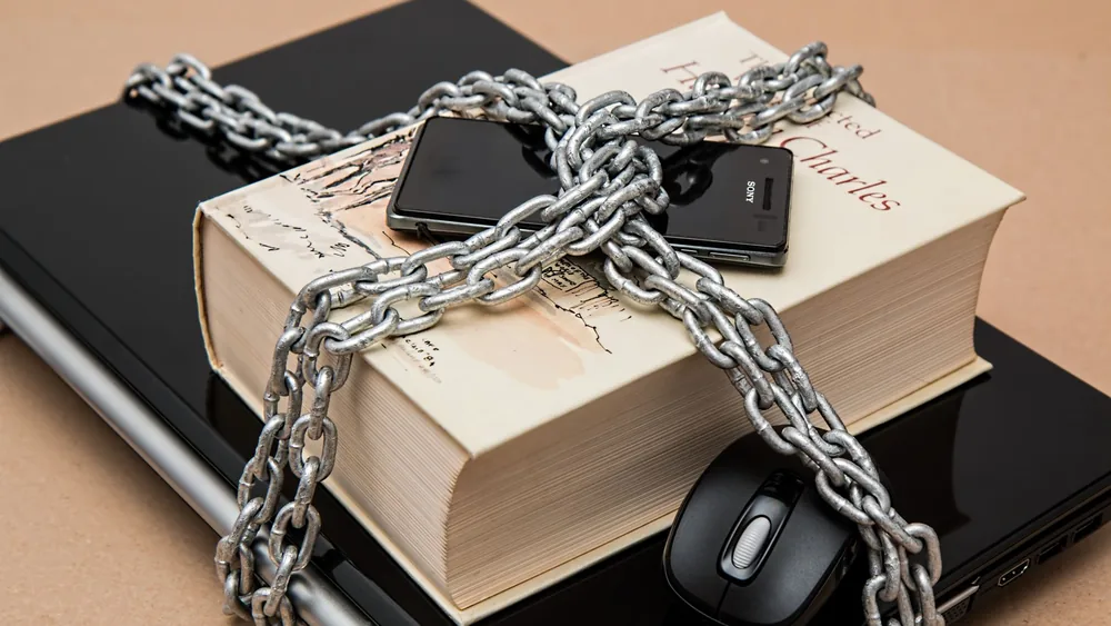 Chain-locked book, phone, and laptop symbolizing digital and intellectual security.
