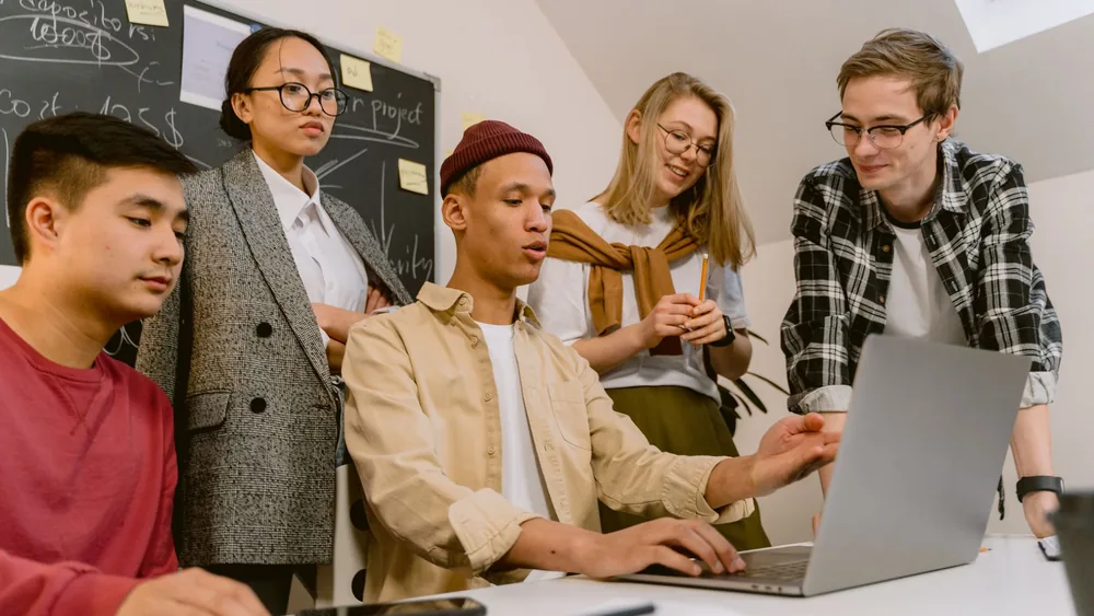 A diverse team of young professionals brainstorming with a laptop in a modern office.