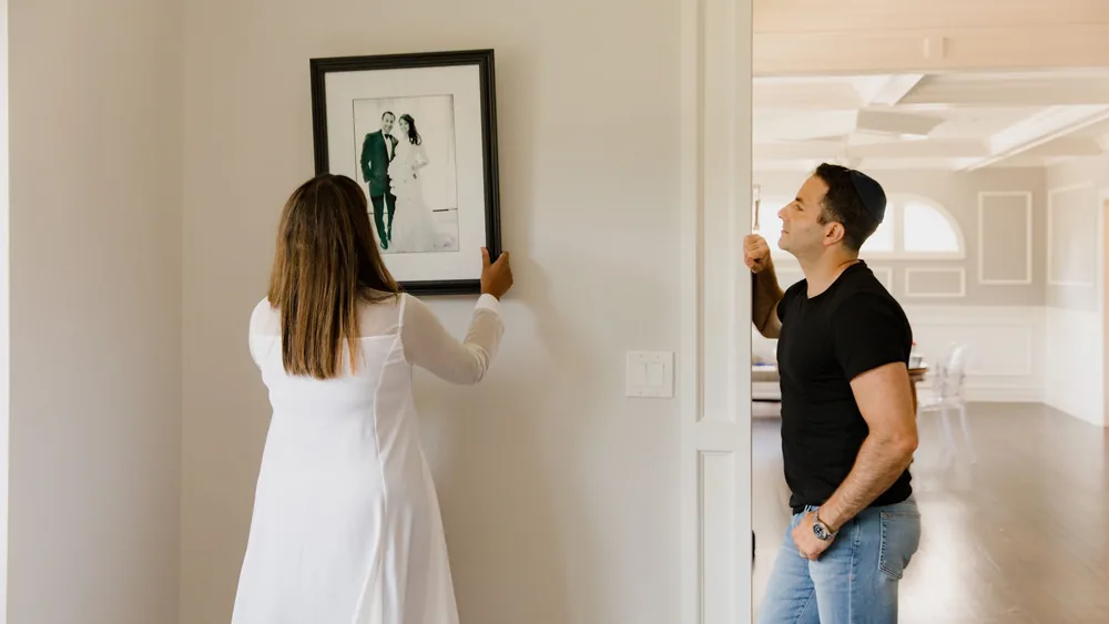 A couple decorates their modern home by hanging a framed photograph on the wall.