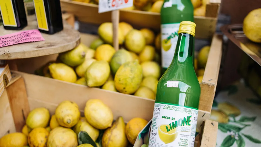 Boxes of fresh lemons with bottles of limone juice at a vibrant market.