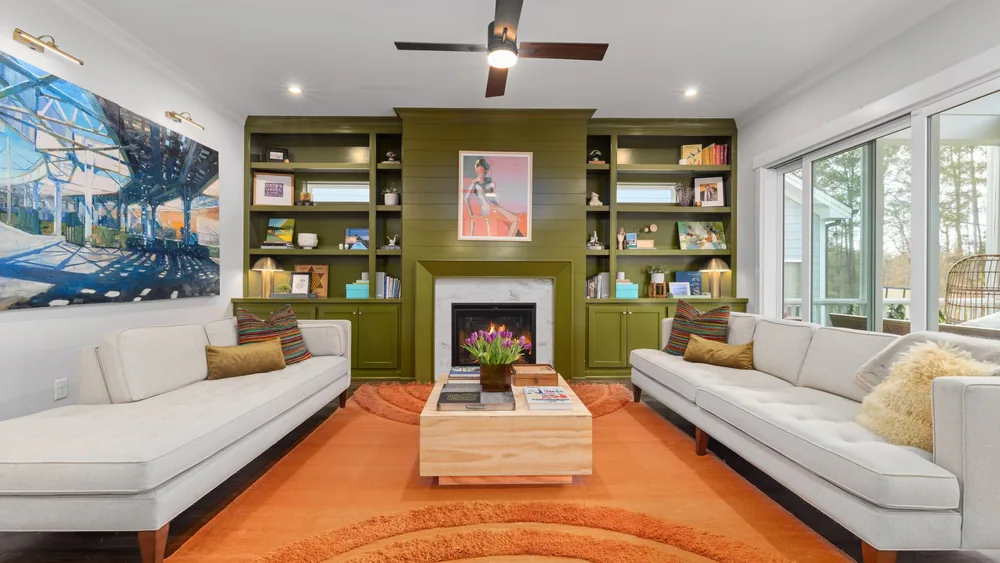 Elegant living room featuring green bookshelves, cozy sofas, and a vibrant orange rug.