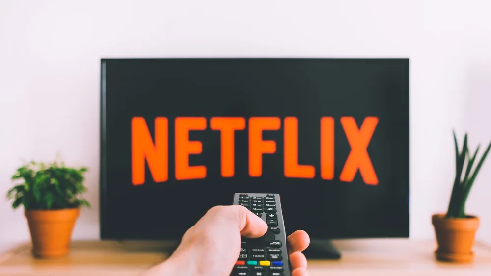 A hand holding a TV remote in front of a screen with Netflix, perfect for streaming and movie night themes.