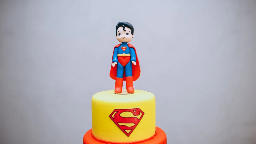 Colorful superhero cake featuring a fondant Superman figurine on top, perfect for themed parties.