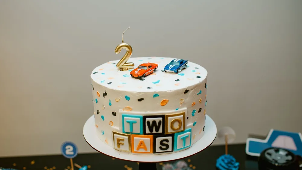 Vibrant birthday cake adorned with toy cars and colorful blocks, perfect for a 2-year-old's celebration.