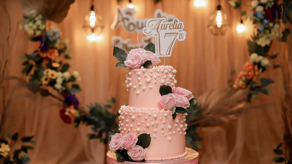 Beautiful pink two-tier birthday cake adorned with roses and pearls, perfect for celebrations.