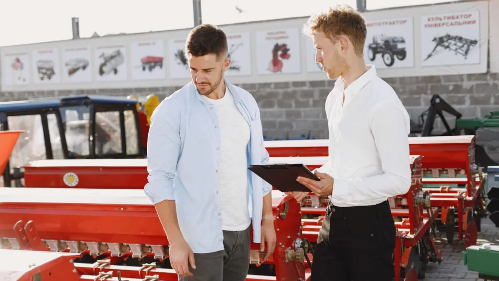 Two men discussing agricultural equipment at an outdoor store during the day.