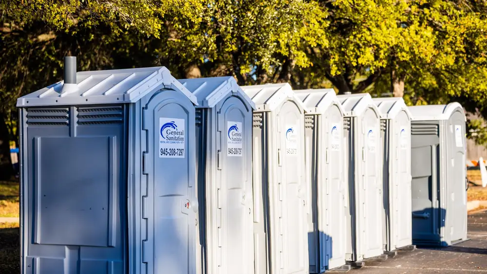 Multiple portable toilets aligned outdoors under trees, creating a sanitation solution.