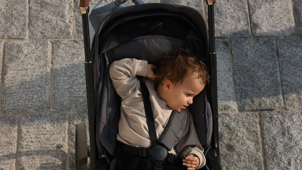 Overhead view of a baby in a stroller on a stone pavement, enjoying a sunny day.