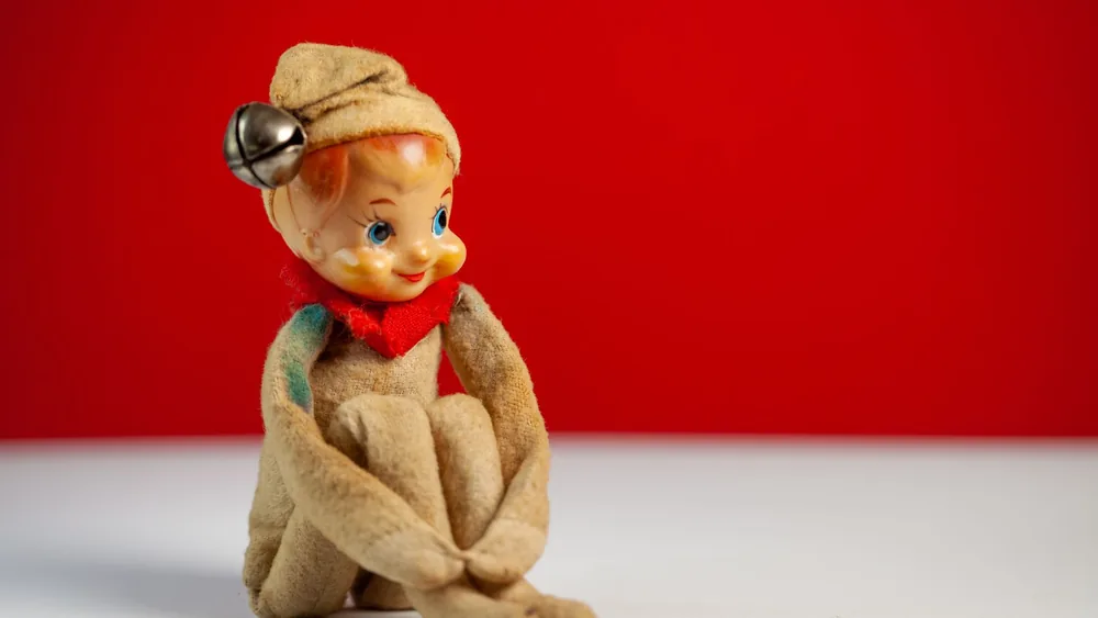Charming vintage doll sitting against a vivid red backdrop.