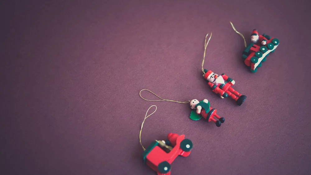 A minimalist flat lay of Christmas ornaments featuring Santa and toys on a purple background.