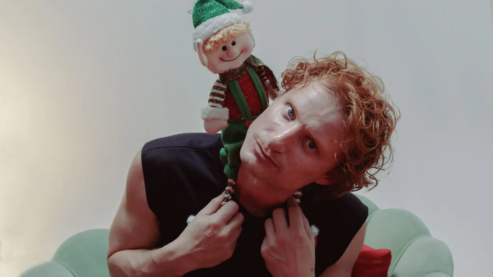 Quirky portrait of a man with a festive elf toy on his shoulder, indoors.