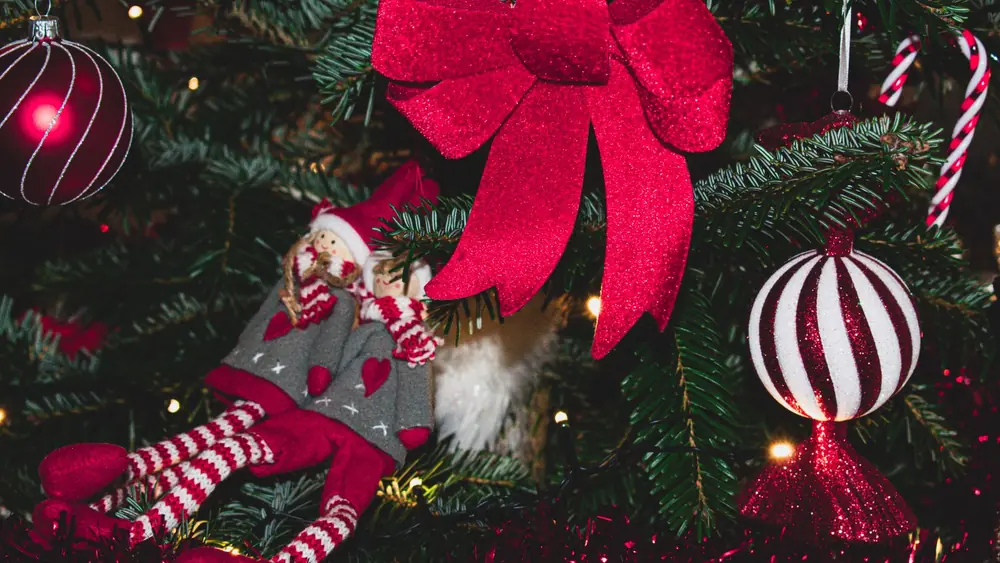 Close-up of vibrant Christmas tree ornaments with a red bow, capturing holiday spirit.