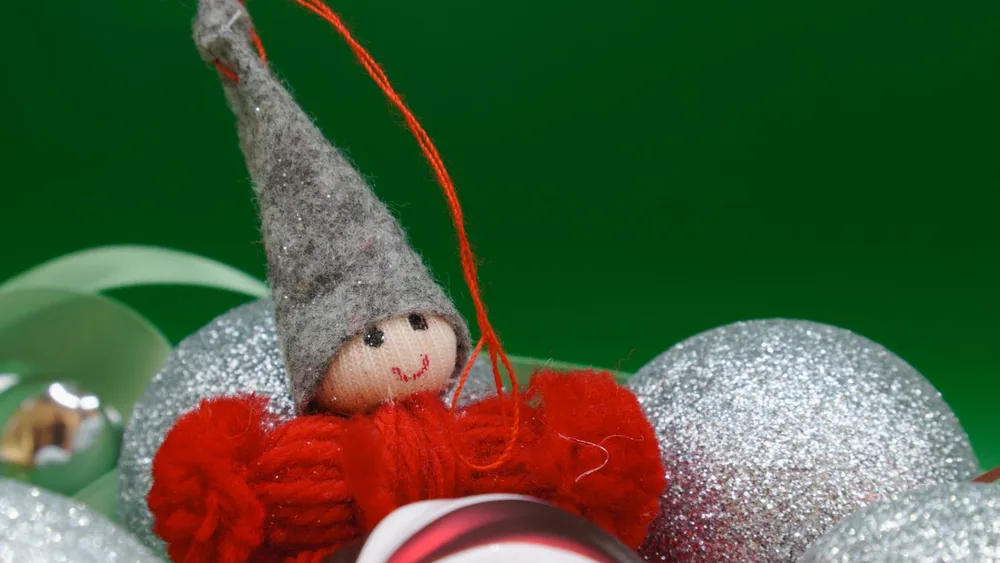 A cheerful elf Christmas ornament surrounded by glittery holiday decorations.