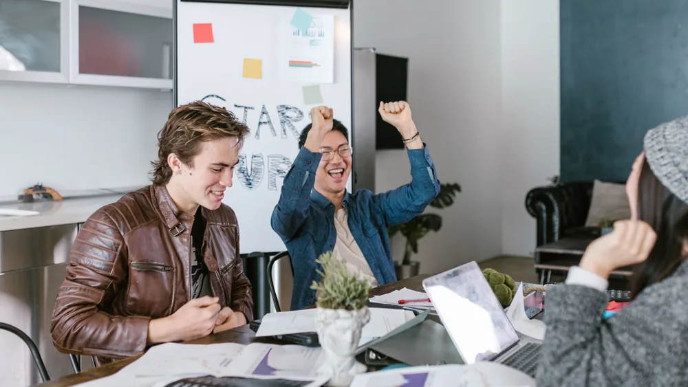 A group of diverse colleagues joyfully celebrate a successful meeting in a modern office setting.