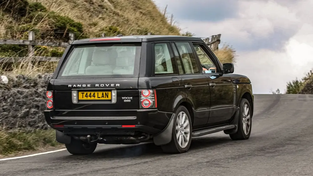 Black Range Rover cruising through a picturesque mountain road, epitomizing travel adventure.
