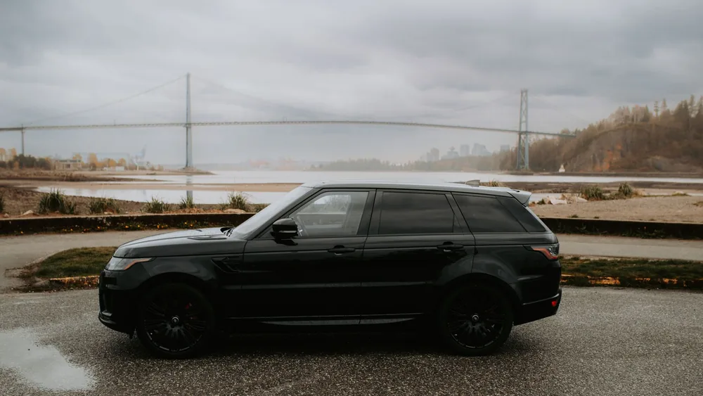 Black SUV parked near Lions Gate Bridge in cloudy Vancouver atmosphere.