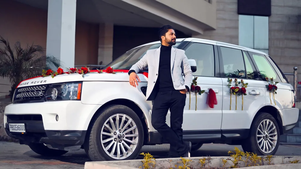 Fashionable man in a blazer leaning on a flower-adorned Range Rover in Amritsar.