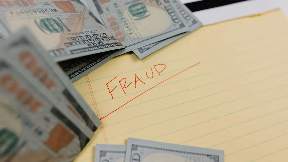 Close-up of US dollars and 'Fraud' written on yellow paper, representing financial scams.