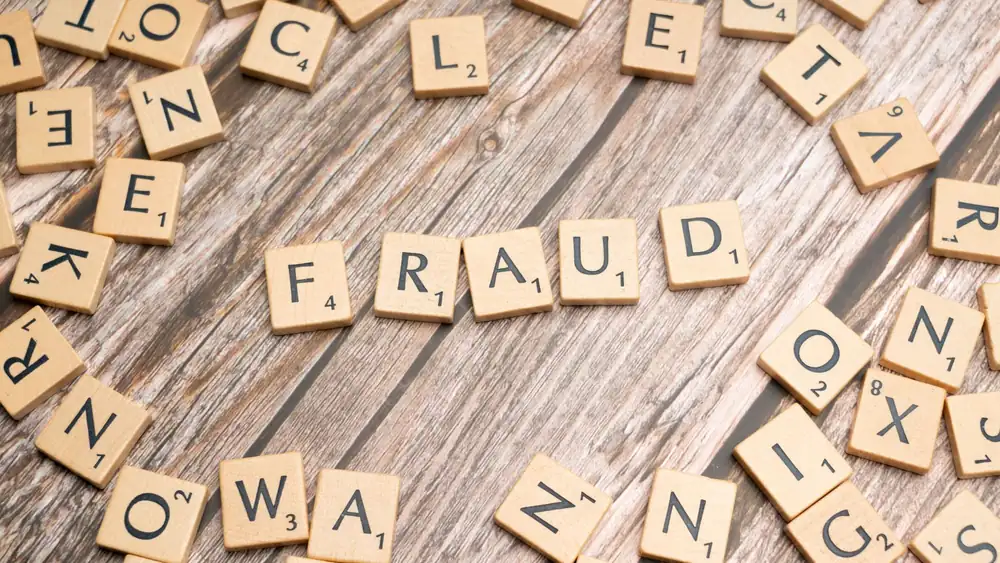 Alphabet tiles arranged to spell 'fraud' on a wooden surface, symbolizing deception.