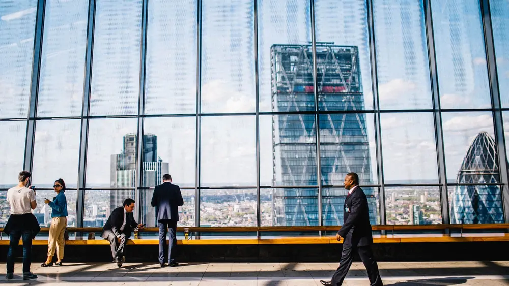Business professionals in a modern office against a London skyline view.