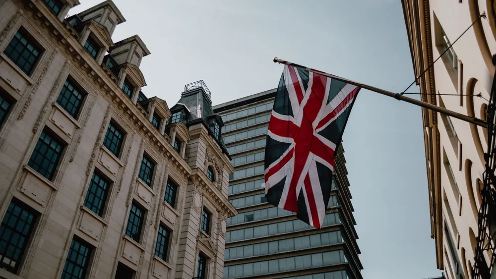 Low angle view of a Union Jack flag with historic and modern buildings in London, UK.