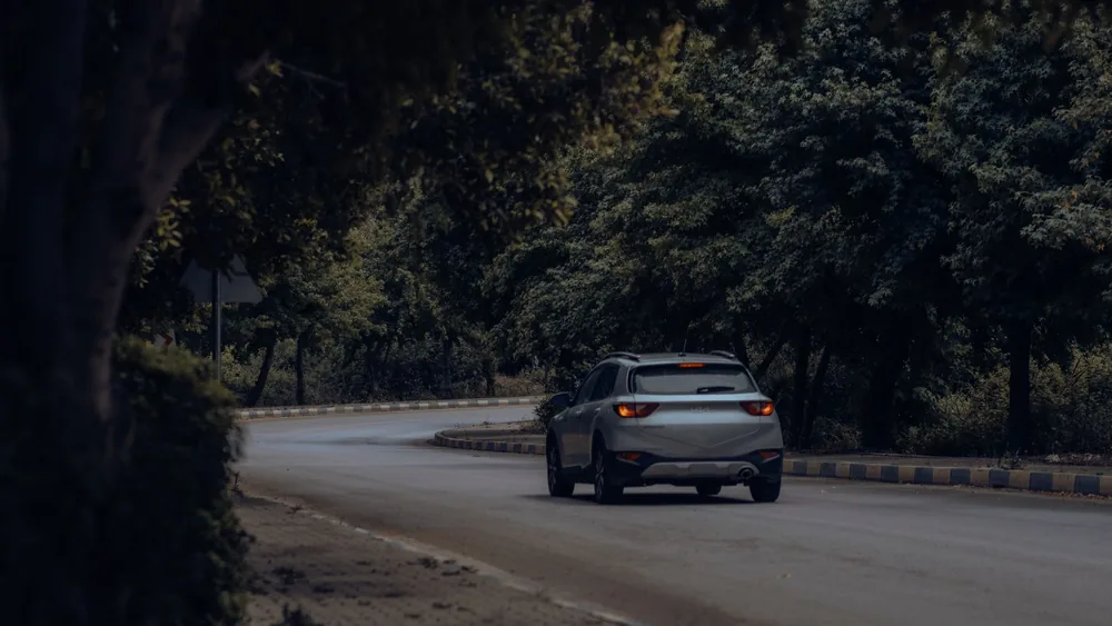 A silver SUV navigates a winding road through a dense forest. Captured during the day.