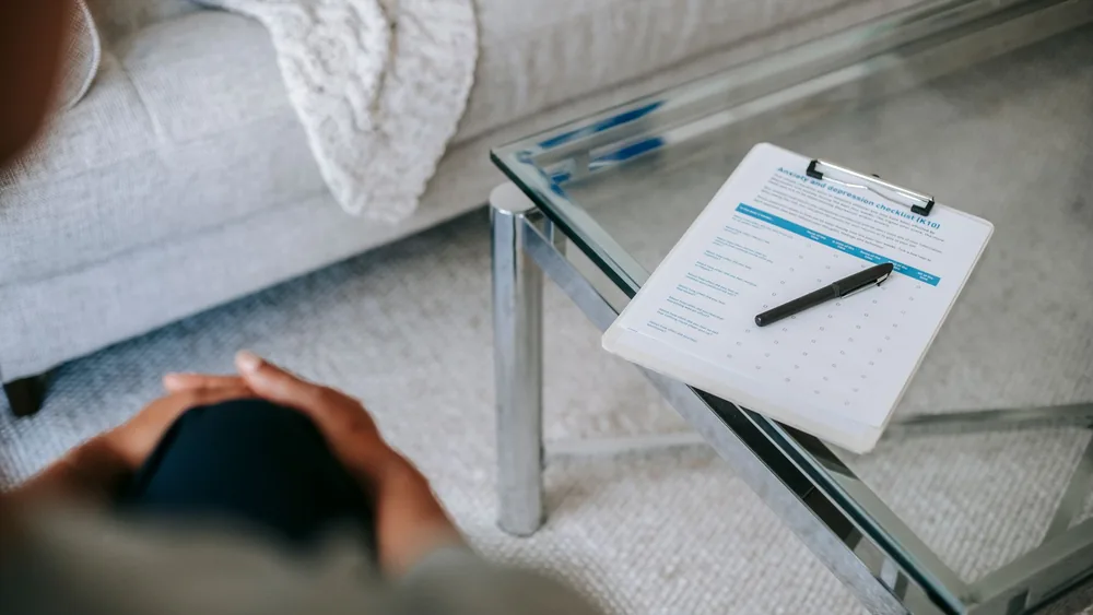 From above of blurred unrecognizable female psychologist sitting in office near table with clipboard and pen during session in office