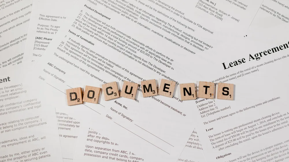Top view of scrabble tiles spelling 'DOCUMENTS' on various contracts and agreements.