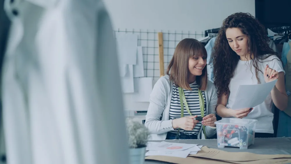 Two women discussing designs in a fashion studio, collaborating over sewing patterns.