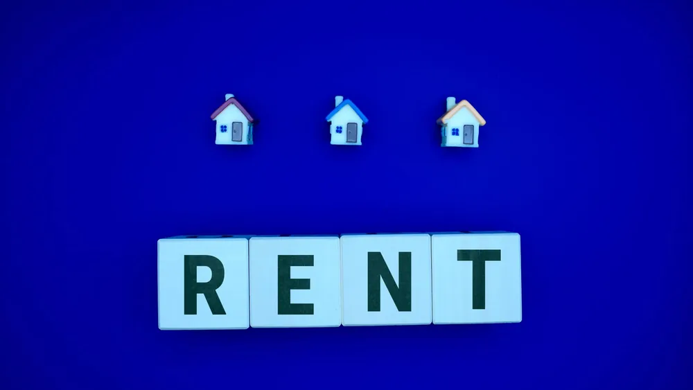 Miniature houses above letters spelling 'RENT' on a blue background, ideal for real estate themes.