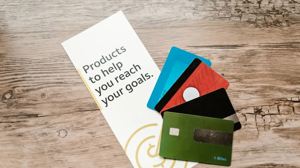 Assorted credit cards on a wooden table next to a leaflet with motivational text about financial goals.