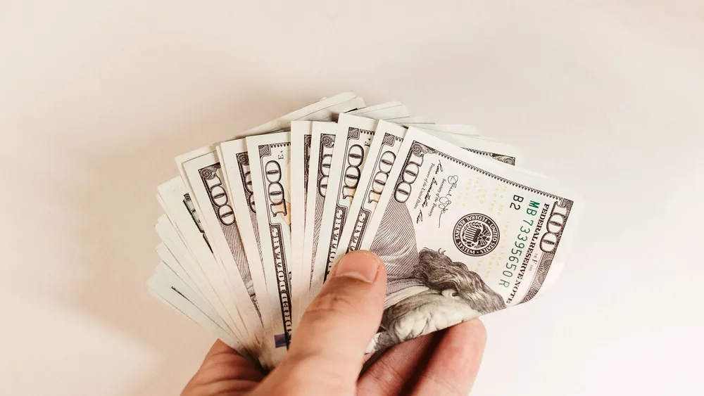 Close-up of a hand holding US hundred-dollar bills on a white background.
