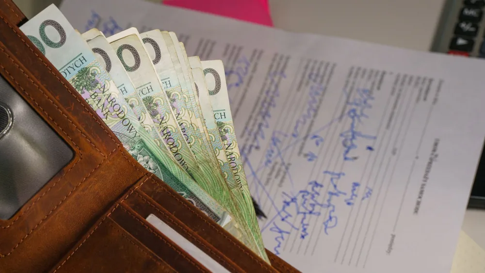 Close-up of a wallet containing Polish Zloty with a signed document in the background, representing financial transactions.
