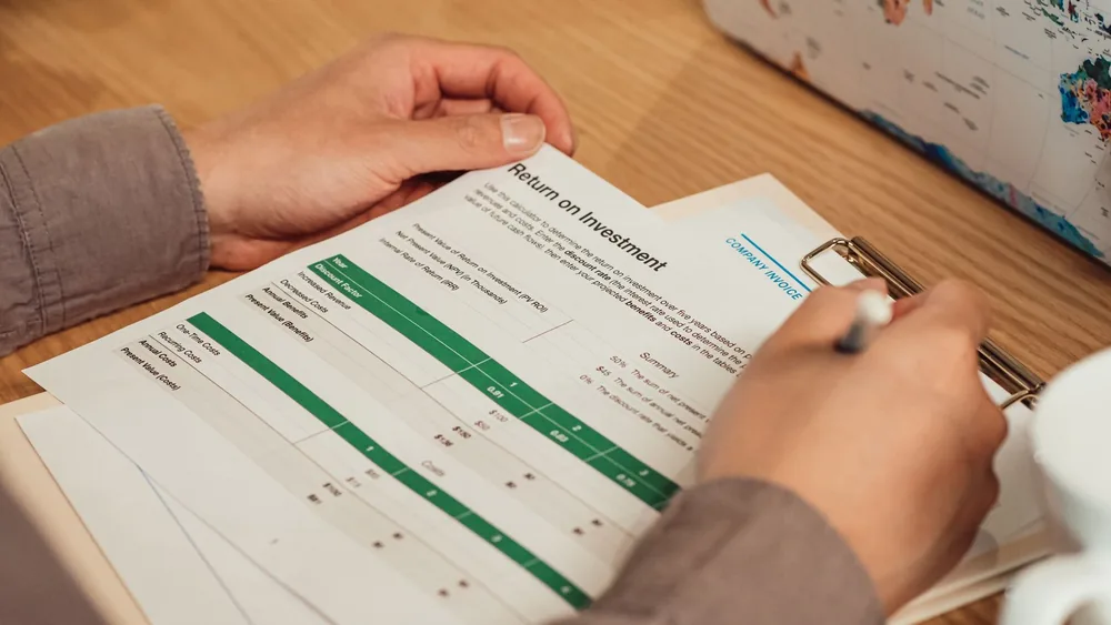 A person analyzing a return on investment report with a pen in hand on a desk.