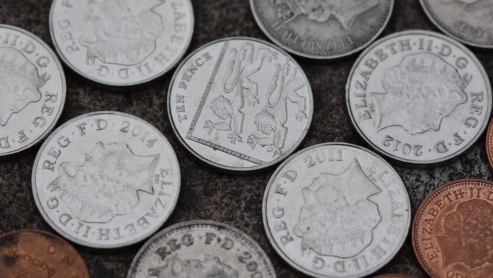 Close-up image of various British coins on a textured stone surface.