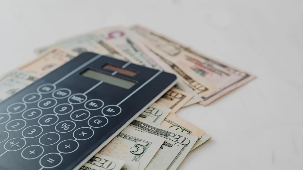 A close-up of a calculator and US dollar banknotes, symbolizing financial calculation and budgeting.