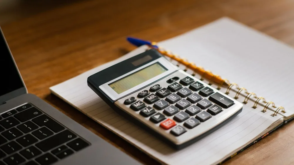 Calculator and open laptop on wooden desk, ideal for financial or accounting tasks.