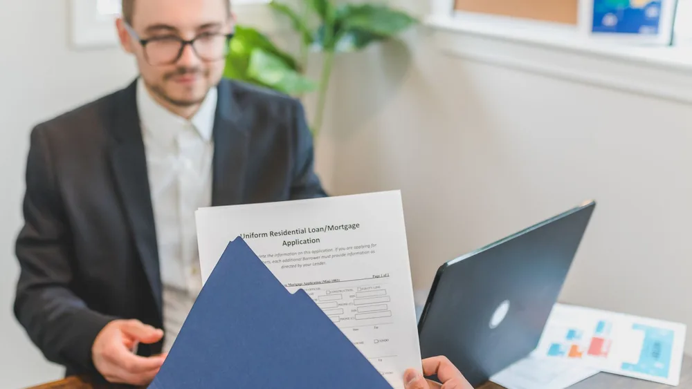 Mortgage broker and client discussing loan application with documents on table.