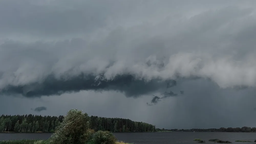 A powerful storm cloud formation looms over a tranquil lake and forest, capturing nature's dynamic beauty.