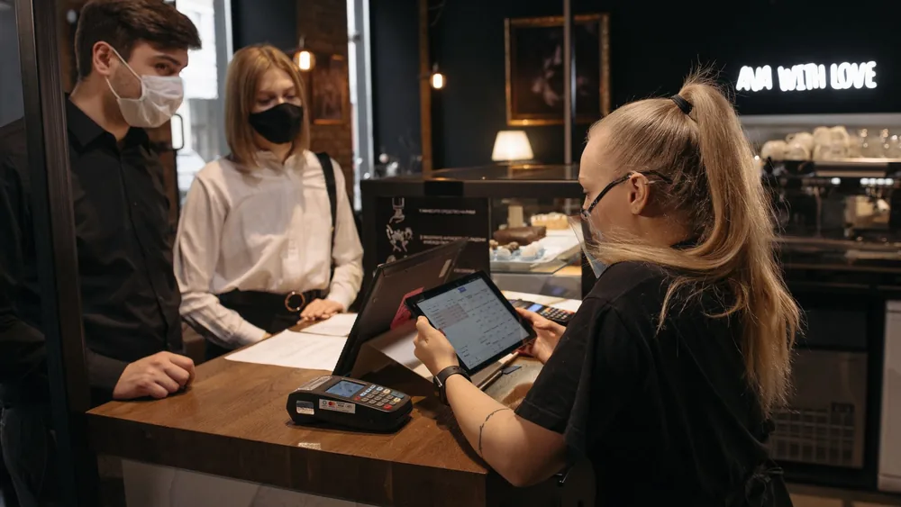 Customers place an order at a café counter with a barista using a tablet for payment.