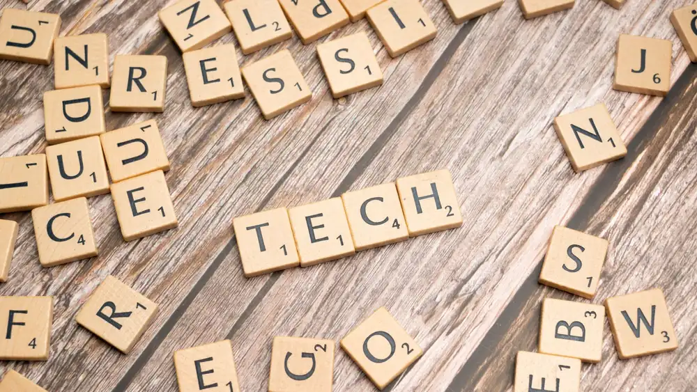 Wooden Scrabble tiles spelling 'TECH' on a textured surface, showcasing creativity.