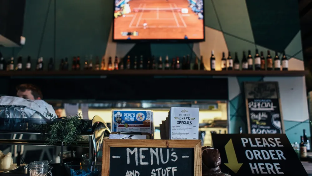 A lively bar scene with menus and bottles, featuring a TV showing sports.