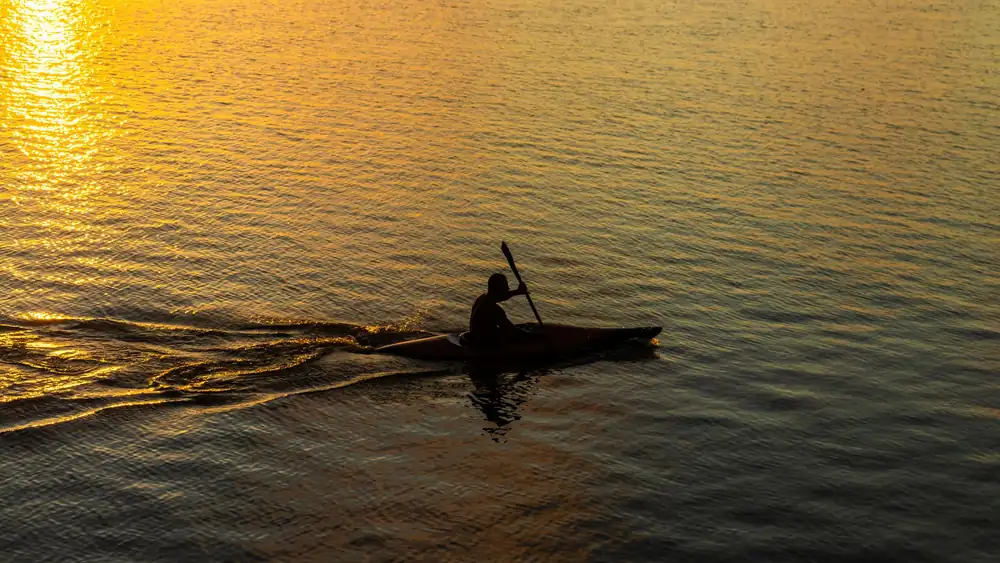 A kayaker paddling in silhouette against a stunning sunset on Brazilian waters, creating a tranquil scene.