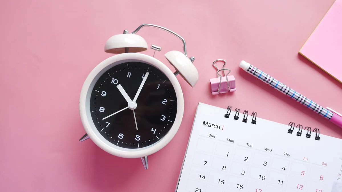 A planner and clock on a desk, used to manage a working day