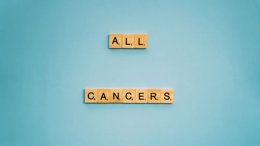 Scrabble tiles forming 'All Cancers' on a light blue background, symbolizing cancer awareness.